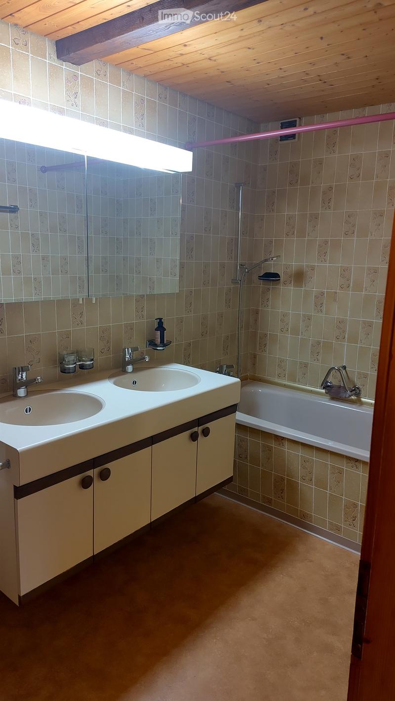 Bathroom with double sink, bathtub, and tiled walls. Features a wooden ceiling and warm lighting.