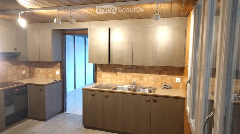 Modern kitchen with wooden cabinets, stainless steel sink, and built-in oven. Features pendant lighting and a large window providing natural light.