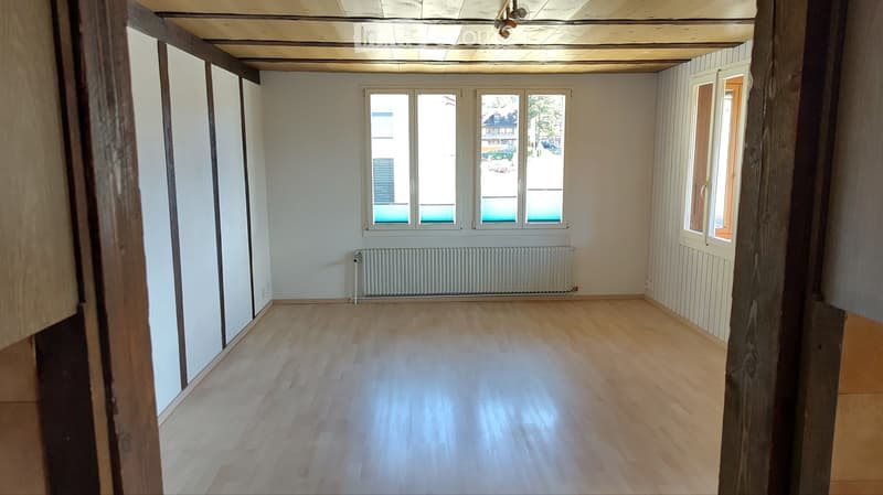 Empty room with wooden flooring, white walls, large windows, and a radiator. No furniture or equipment present.