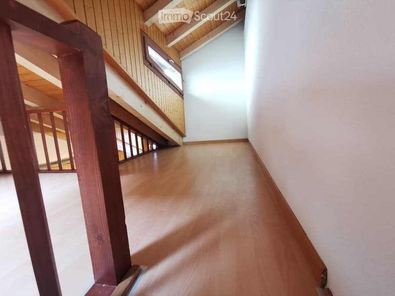 Empty hallway with wooden flooring, white walls, and a wooden staircase with a railing leading upwards.