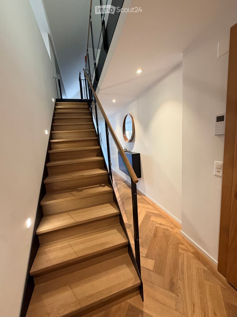 Modern staircase with wooden steps and a sleek metal railing, illuminated by recessed lighting, leading to an upper level.