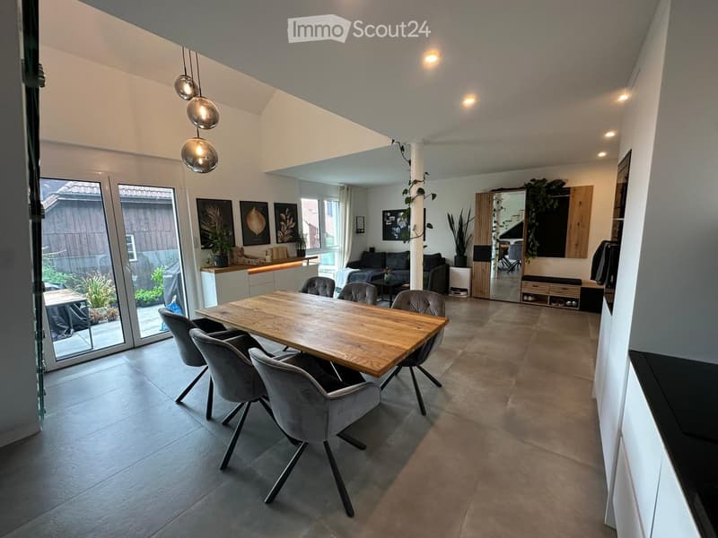 Open-plan living and dining area with modern furniture, large windows, and pendant lights.