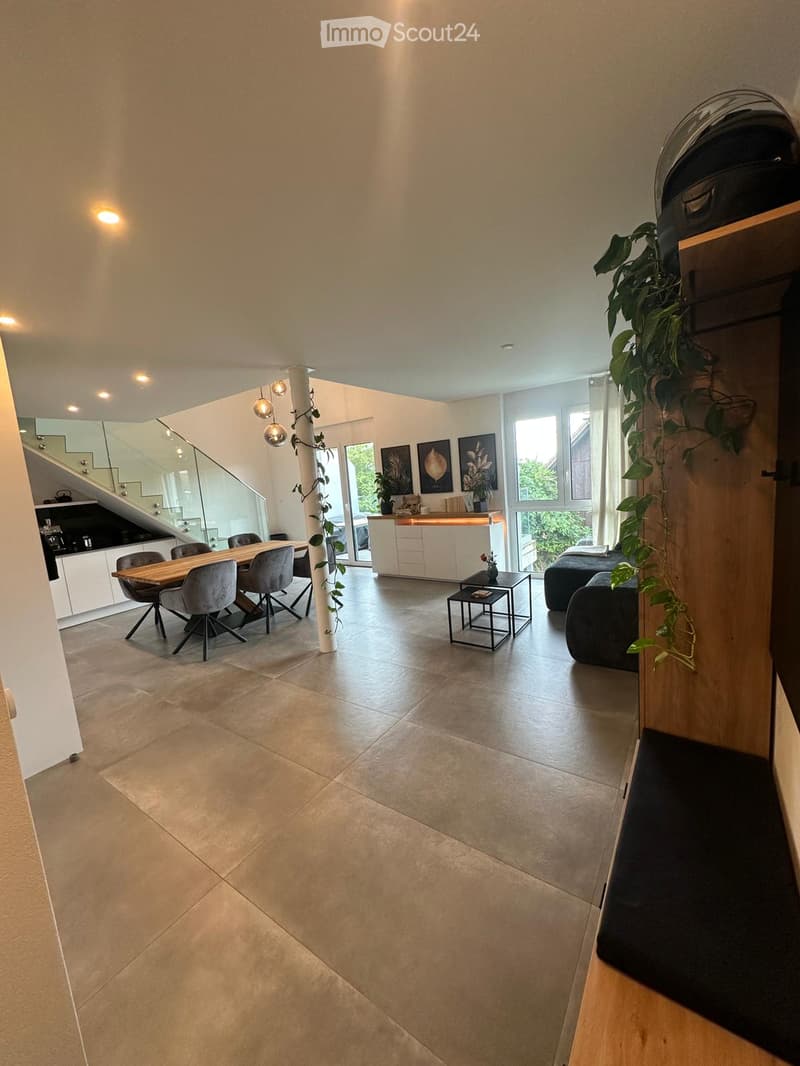 Open-plan living and dining area with modern furniture, large windows, and a staircase leading to another level.
