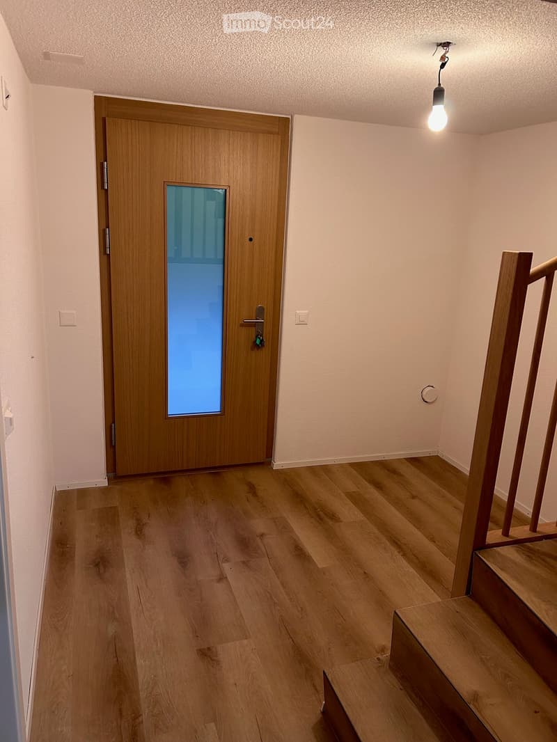 Empty hallway with wooden flooring, a wooden door with a glass panel, and a staircase leading upwards.