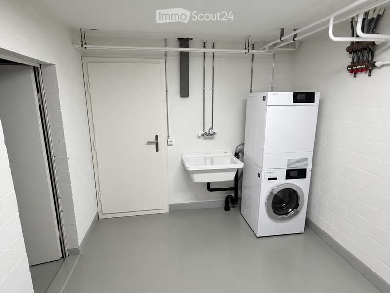 Modern bathroom with white brick walls, grey floor, white washing machine, and a small sink.