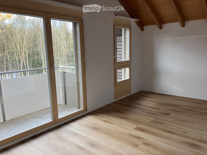 Empty room with wooden flooring, large sliding glass doors leading to a balcony, and a slanted wooden ceiling.