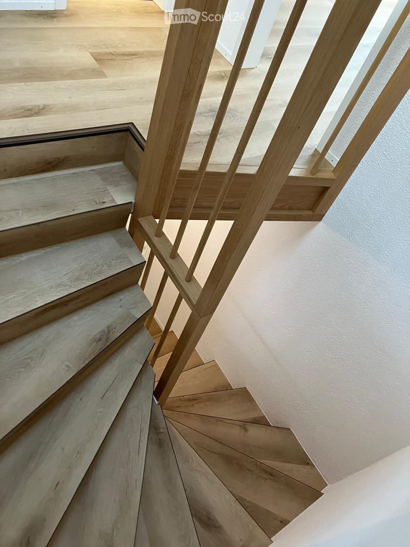 Wooden staircase with modern balustrade, light-colored wooden steps, and a light-colored wall in the background.