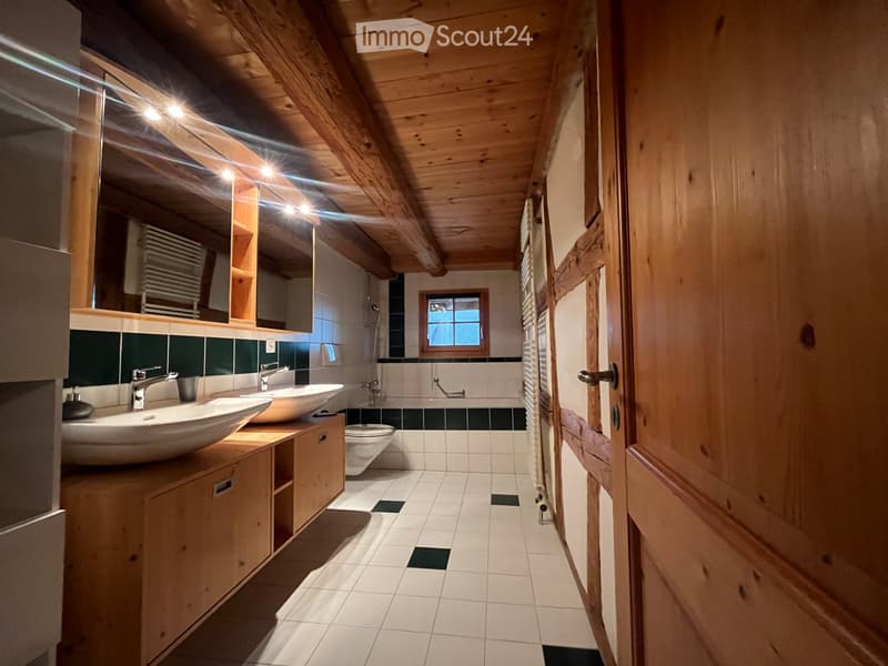 Modern bathroom with wooden beams, white tiles, double sinks, a bathtub, and a window letting in natural light.
