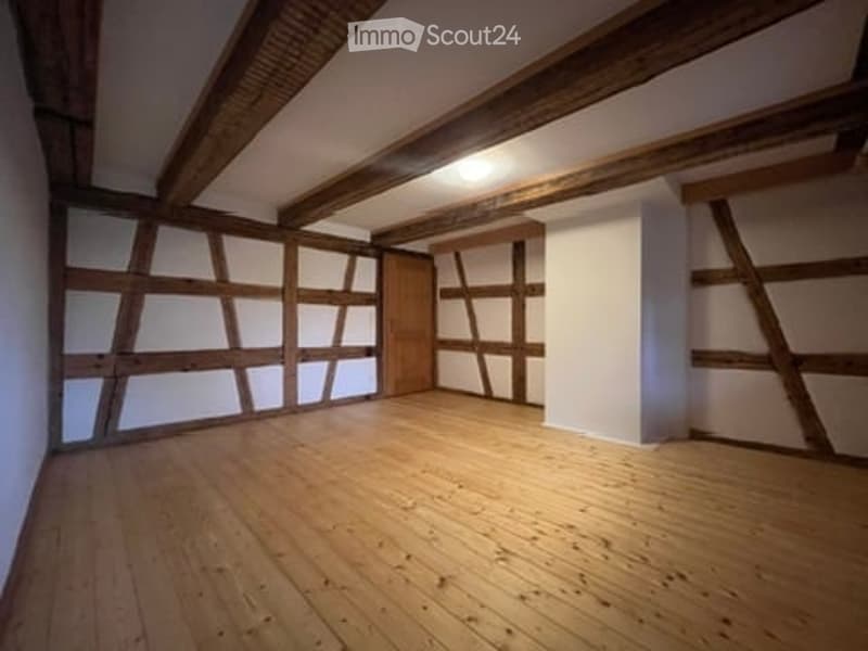 Empty room with exposed wooden beams, white plaster walls, and wooden floor. No furniture or equipment.