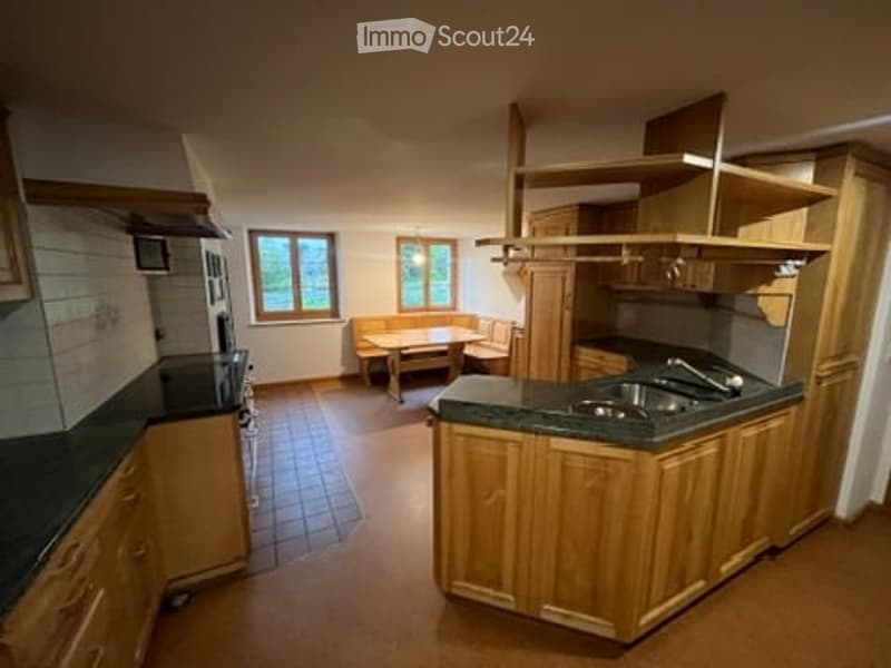 Bright kitchen with wooden cabinets, granite countertop, sink, and a small dining area with a table and chairs.