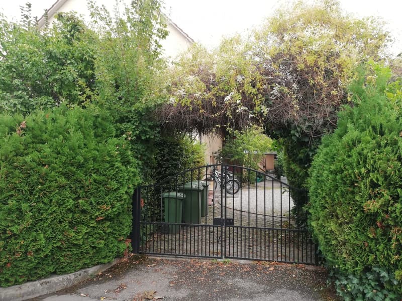 Entrance gate leading to a gravel driveway, bicycles parked beside the gate, greenery all around
