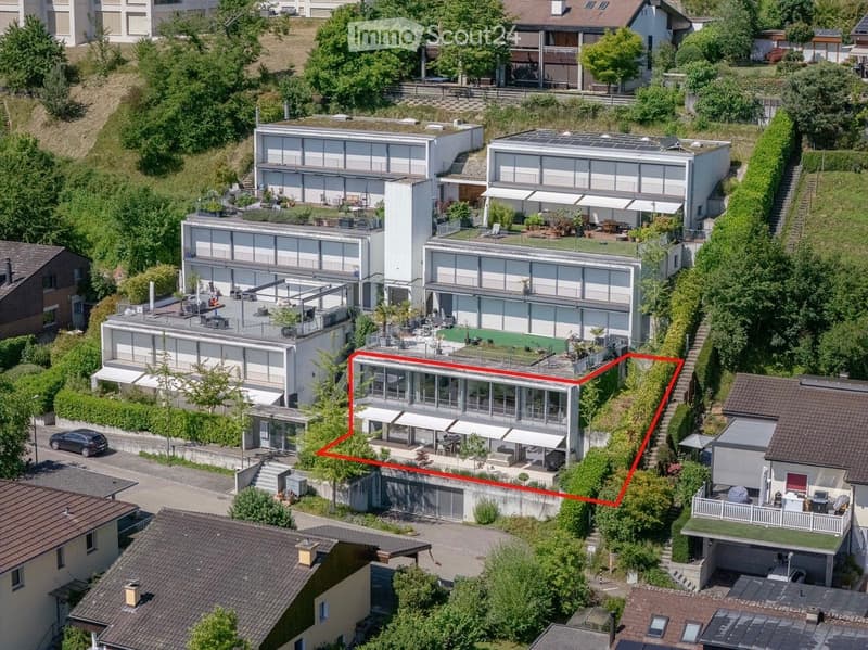Aerial view of a modern, multi-story residential complex with large glass windows, terraces, and surrounding greenery.