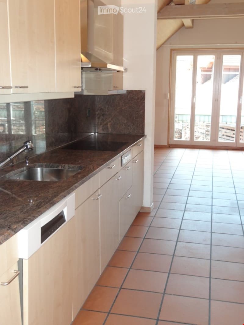 Modern kitchen with white cabinets, granite countertop, stainless steel sink, dishwasher, and range hood. Large sliding glass doors lead to a balcony.