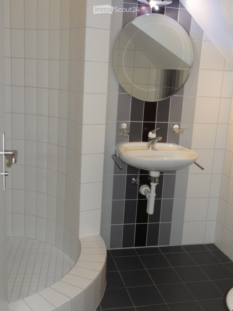 Modern bathroom with white tiled walls, black tiled floor, a white sink with a chrome faucet, a round mirror, and a soap dispenser.
