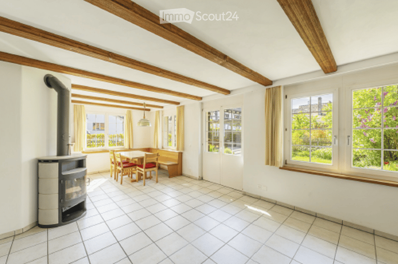 Bright room with exposed wooden beams, fireplace, dining table with chairs, and bench seating.