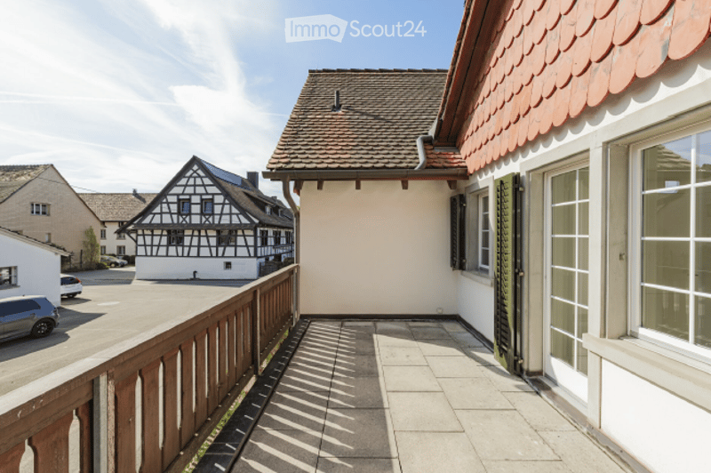 Balcony with wooden railing, tiled floor, and view of neighboring houses and parked cars.
