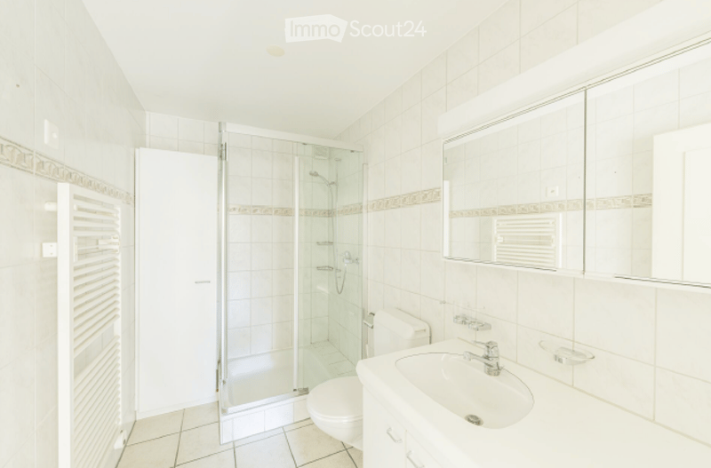 Modern bathroom with white tiles, a glass-enclosed shower, a sink with a mirror, and a toilet.