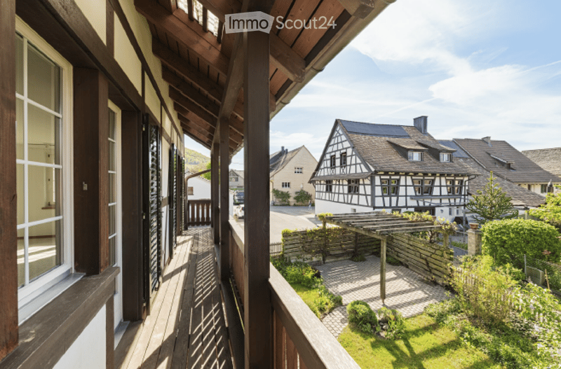 Balcony overlooking a quaint village with traditional half-timbered houses, wooden railings, and a small garden area below.