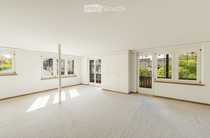 Completely empty room with white walls, large windows, and a white column in the center. No furniture or equipment.