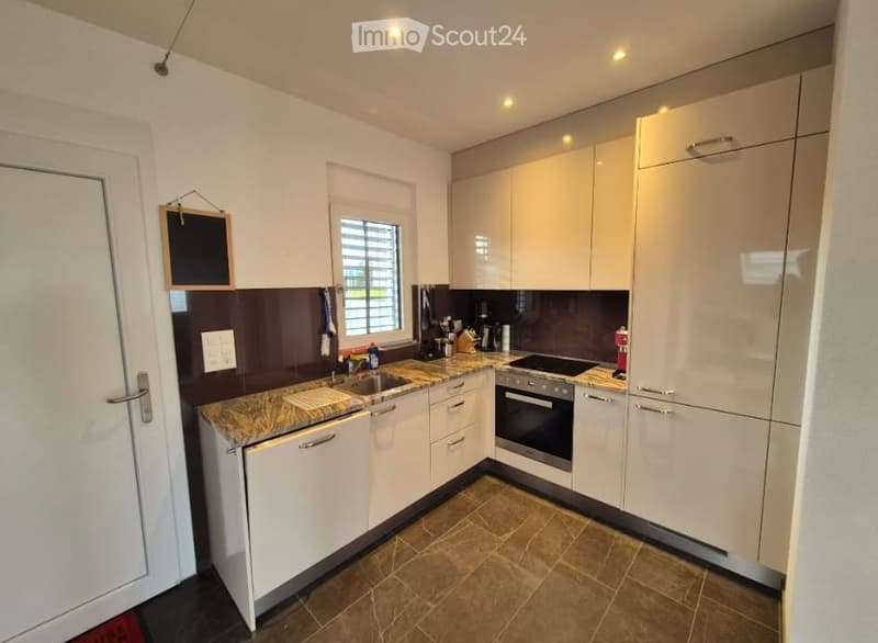 Modern kitchen with white cabinets, marble countertop, built-in oven, sink, and various appliances.