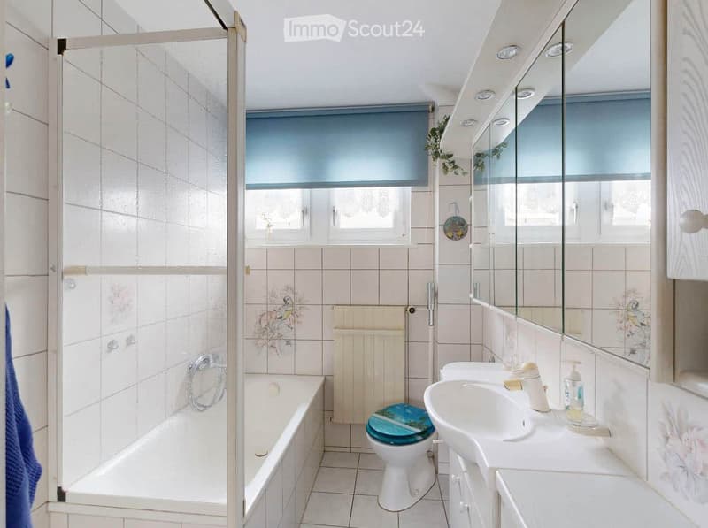 Bathroom with a bathtub, toilet, sink, mirror, radiator, and a glass-enclosed shower stall. The room features tiled walls and floor, with a window above the sink and a towel hanging on the side.