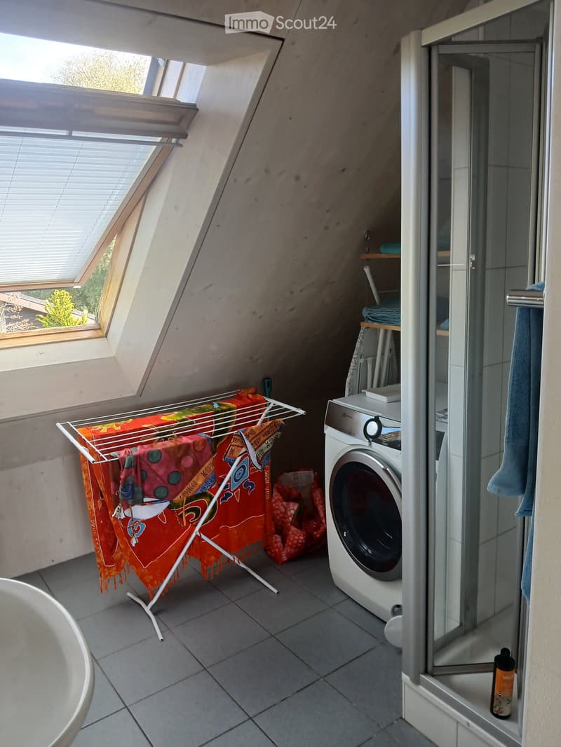 Bathroom with a washing machine, towel rack with colorful towels, shower area, and a small window with blinds.