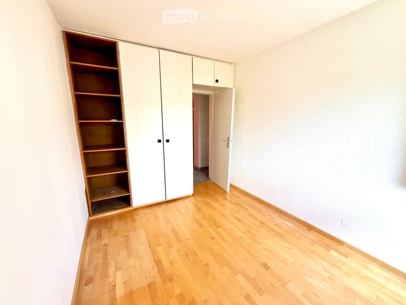Empty room with light wooden flooring, white walls, and built-in white closet with wooden shelves.