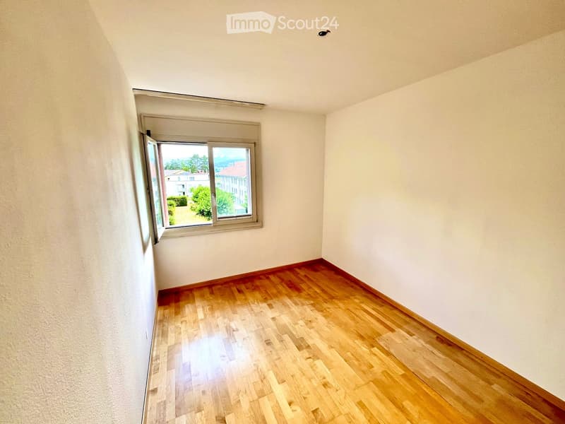 Empty room with wooden flooring and white walls, featuring a large window with a view of the outside.