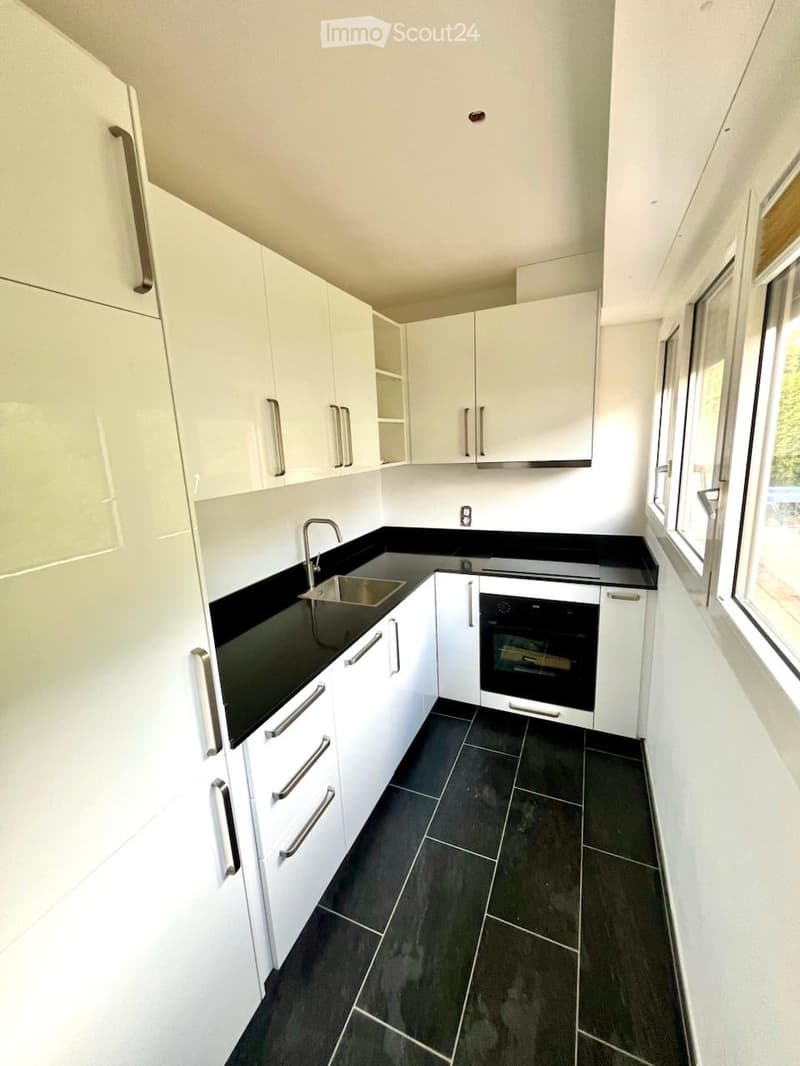 Modern kitchen with white cabinets, black countertops, and dark tiled flooring. Features a sink, oven, and ample storage space.