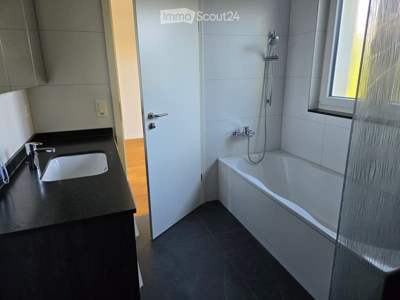 Modern bathroom with a black countertop sink, chrome faucet, bathtub with glass shower enclosure, and a window with a small shelf.