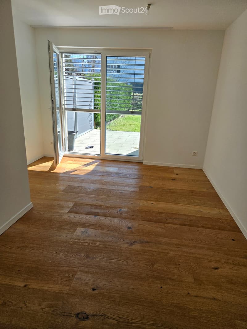 Empty room with wooden flooring, white walls, and large sliding glass doors leading to a patio area.