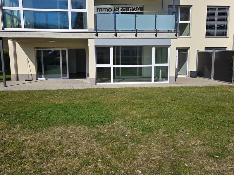 A well-maintained lawn in front of a modern house with large windows, a balcony, and a covered entrance area.