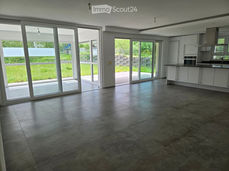 Open-plan space with large sliding glass doors leading to a patio, tiled floor, and a modern kitchen area with white cabinets and stainless steel appliances.