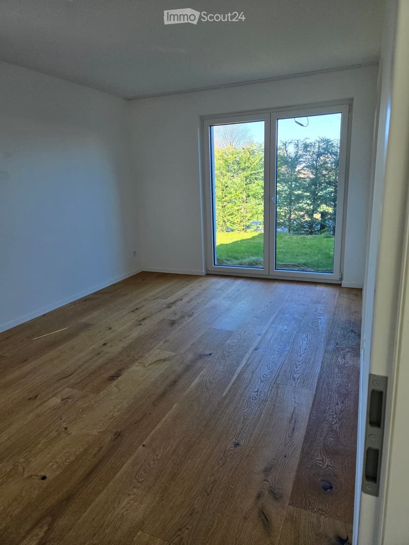 Empty room with wooden flooring and large sliding glass doors leading to a green outdoor area.