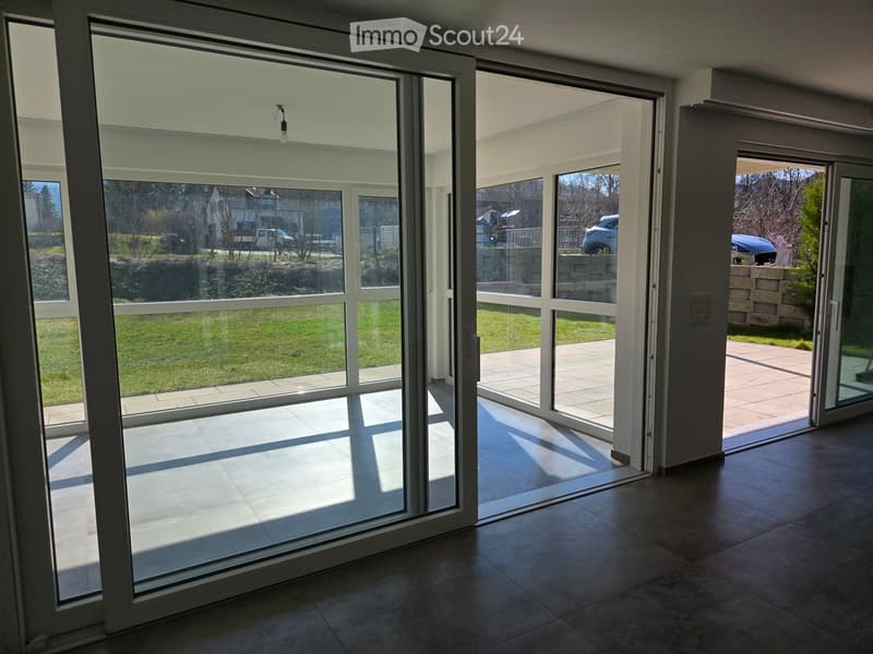 Empty room with large sliding glass doors leading to a patio and garden area. The floor is tiled, and the walls are painted in neutral tones.