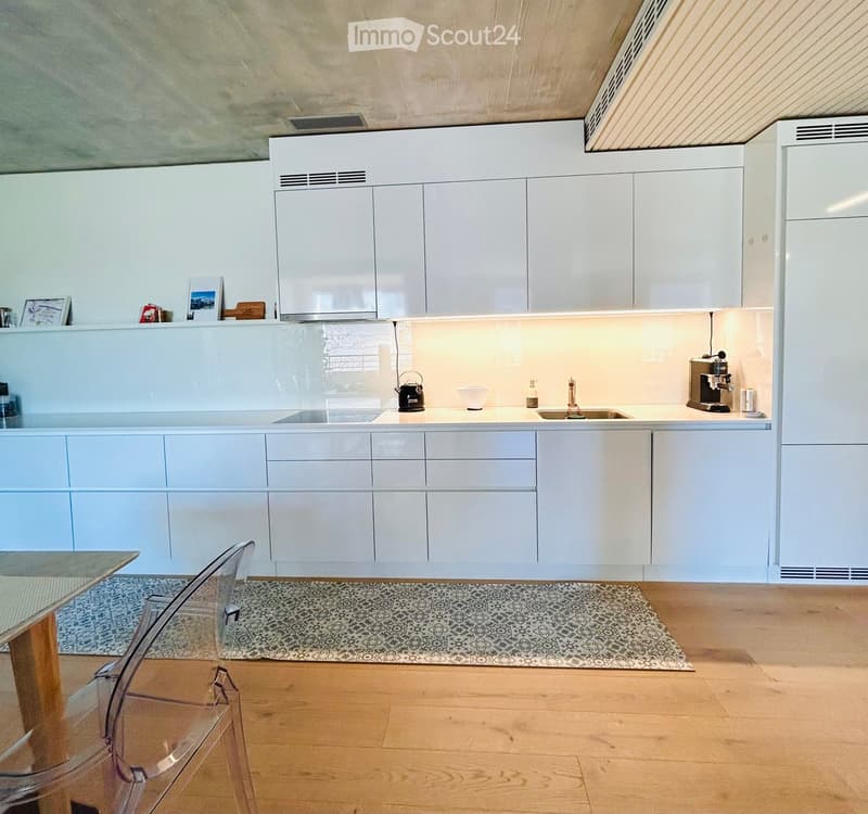 Modern kitchen with white cabinets, a sink, coffee maker, teapot, and a small table with a clear chair.