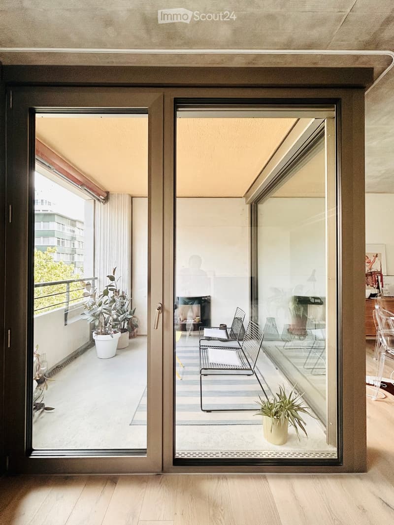 Modern balcony with glass doors, striped floor, metal chairs, small table, and potted plants.