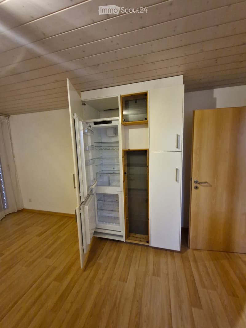 Empty room with wooden flooring, white cabinets, and an open refrigerator. No furniture or personal items are present.