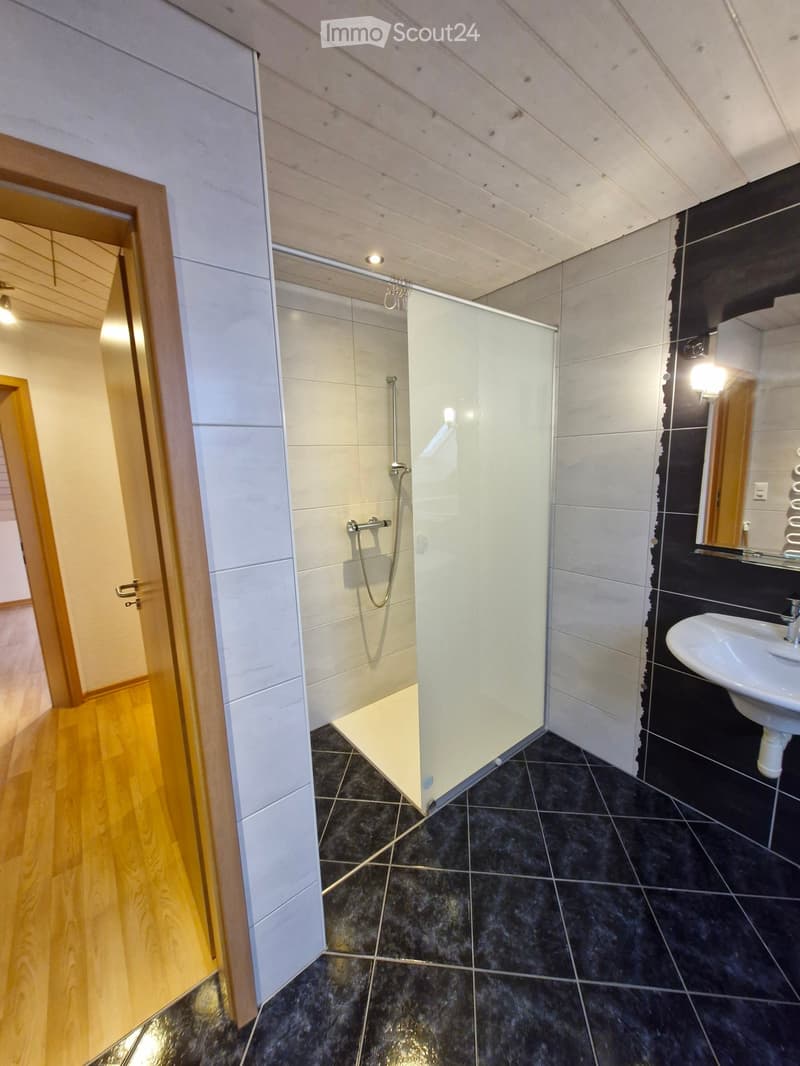 Modern bathroom with black tiled floor, white tiled shower area, sink, and mirror.