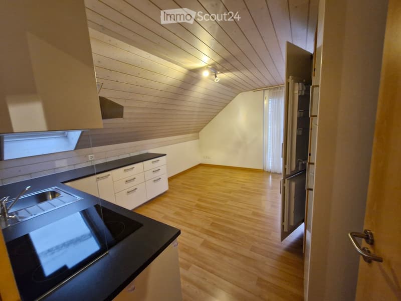 Modern kitchen with white cabinets, black countertop, and wooden flooring. Features a sink, faucet, and an open doorway leading to another room.