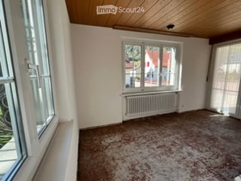 Empty room with wooden ceiling, large windows, radiator, and carpeted floor.