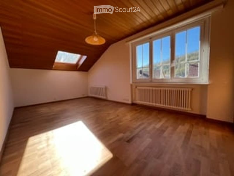 Empty attic room with wooden floors, slanted wooden ceiling, large windows, skylight, radiator, and pendant light fixture.