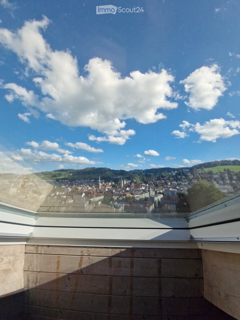 Balcony with wooden decking and panoramic city view under a clear blue sky with scattered clouds.