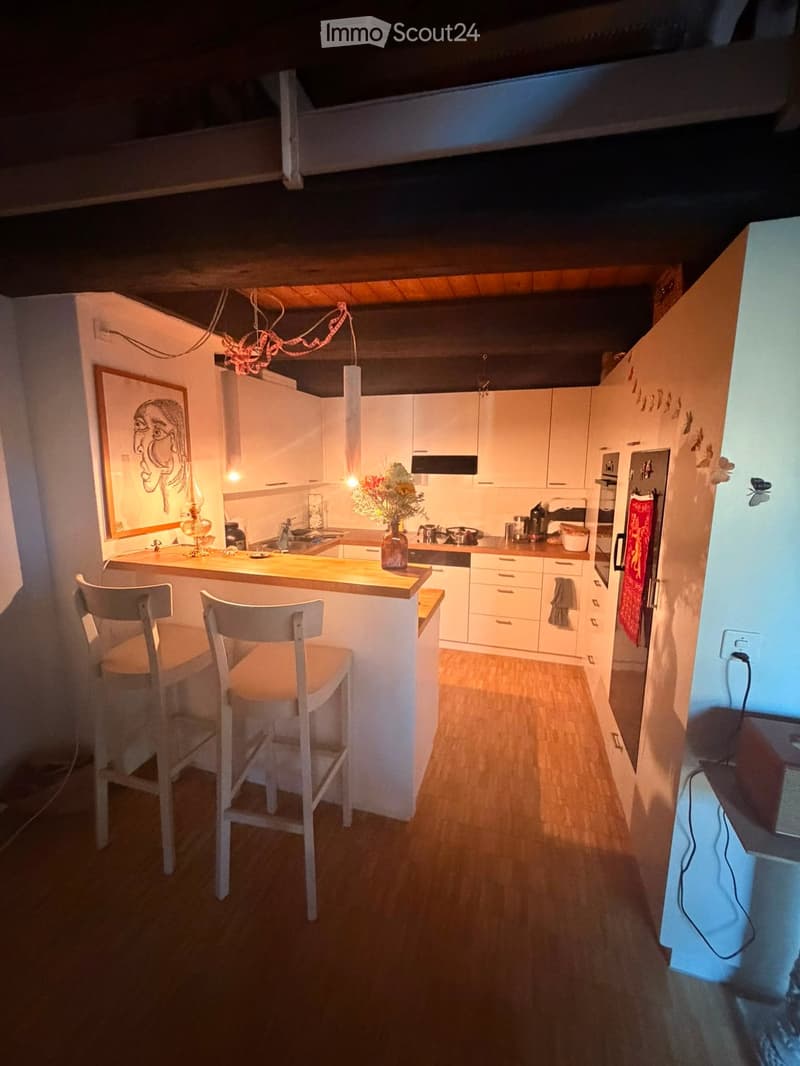 Modern kitchen with white cabinets, wooden island, bar stools, and various appliances.