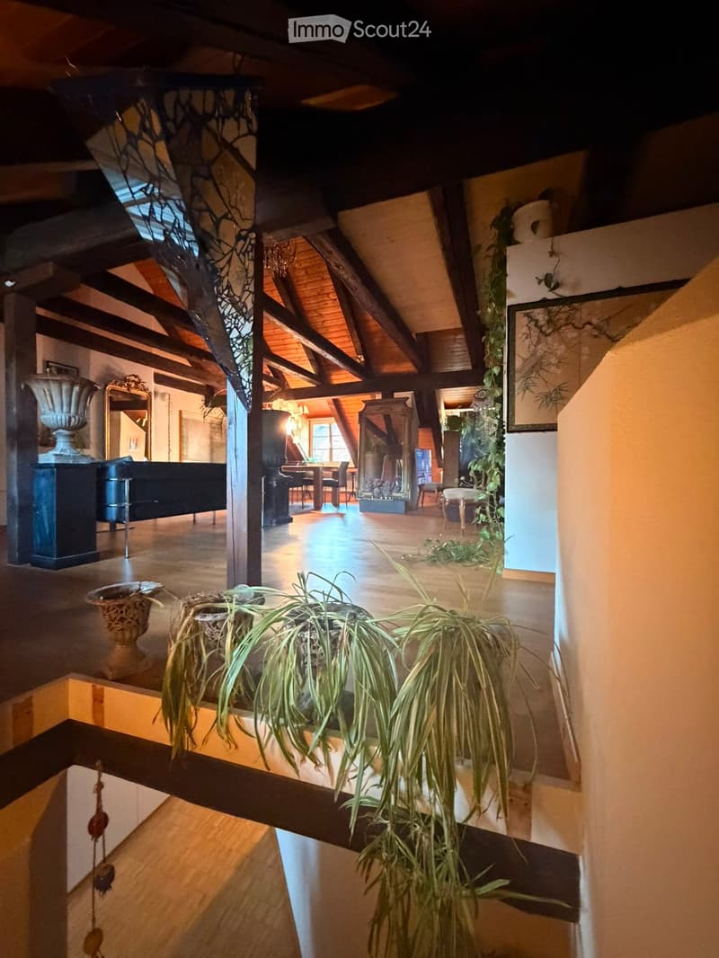 Open-concept living and dining area with wooden floors, exposed wooden beams, a grand piano, a dining table with chairs, and decorative vases.