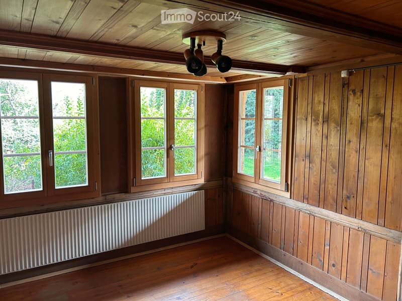 Empty room with wooden walls, wooden ceiling, wooden floor, large windows, radiator, and ceiling lights.