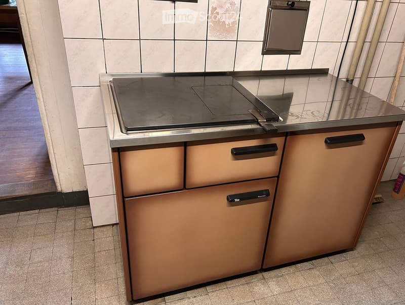 Induction cooktop with cabinets and drawers, tiled walls, and a broom visible in the background.