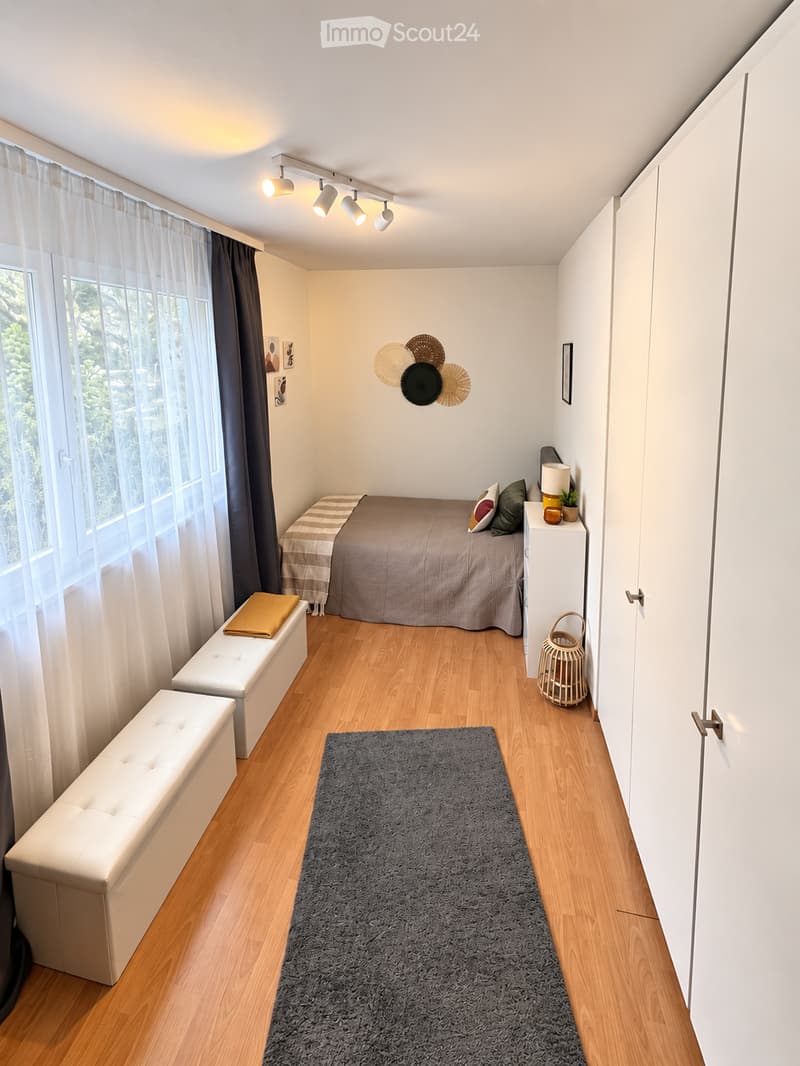 Cozy bedroom with a single bed, two white benches, a nightstand with a lamp, a gray rug, and decorative wall art.