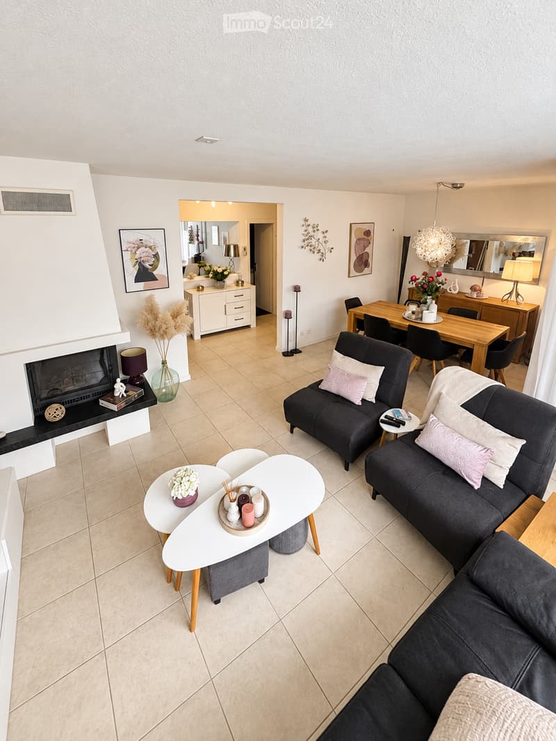 Modern living room with a fireplace, two sofas, a coffee table, side tables, and a dining area with a table and chairs.
