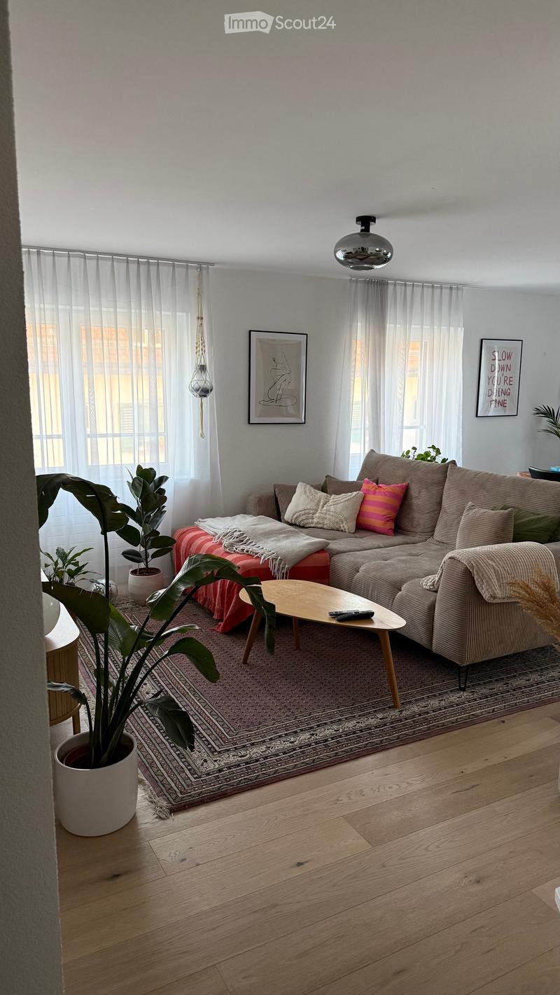 Modern living room with a sectional sofa, coffee table, potted plants, and artwork on the walls.